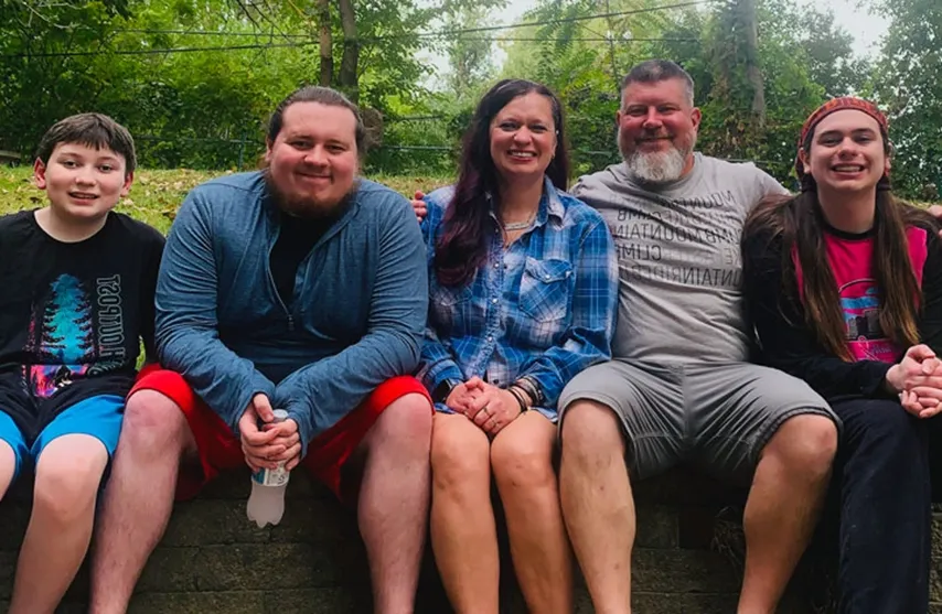 Nichole Plague sits next to her husband and 3 children as they all smile at the camera.