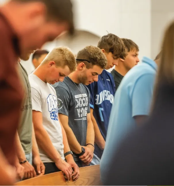 Three students praying during chapel service.